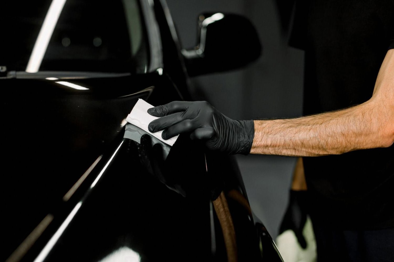 Technician cleaning fine scratches on a black car door in a Dubai detailing bay